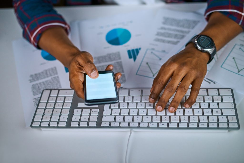 Double-checking the information. High angle shot of an unrecognizable man using his cellphone while sitting at his desk in the office.